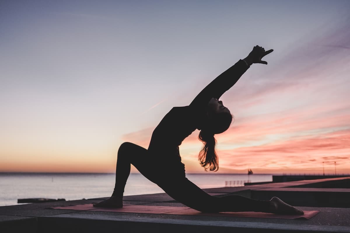Silhouette of a person in a yoga pose at sunset by the sea