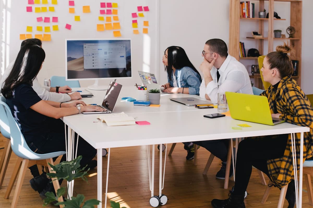 A team collaborating around a table with laptops and sticky notes on the wall