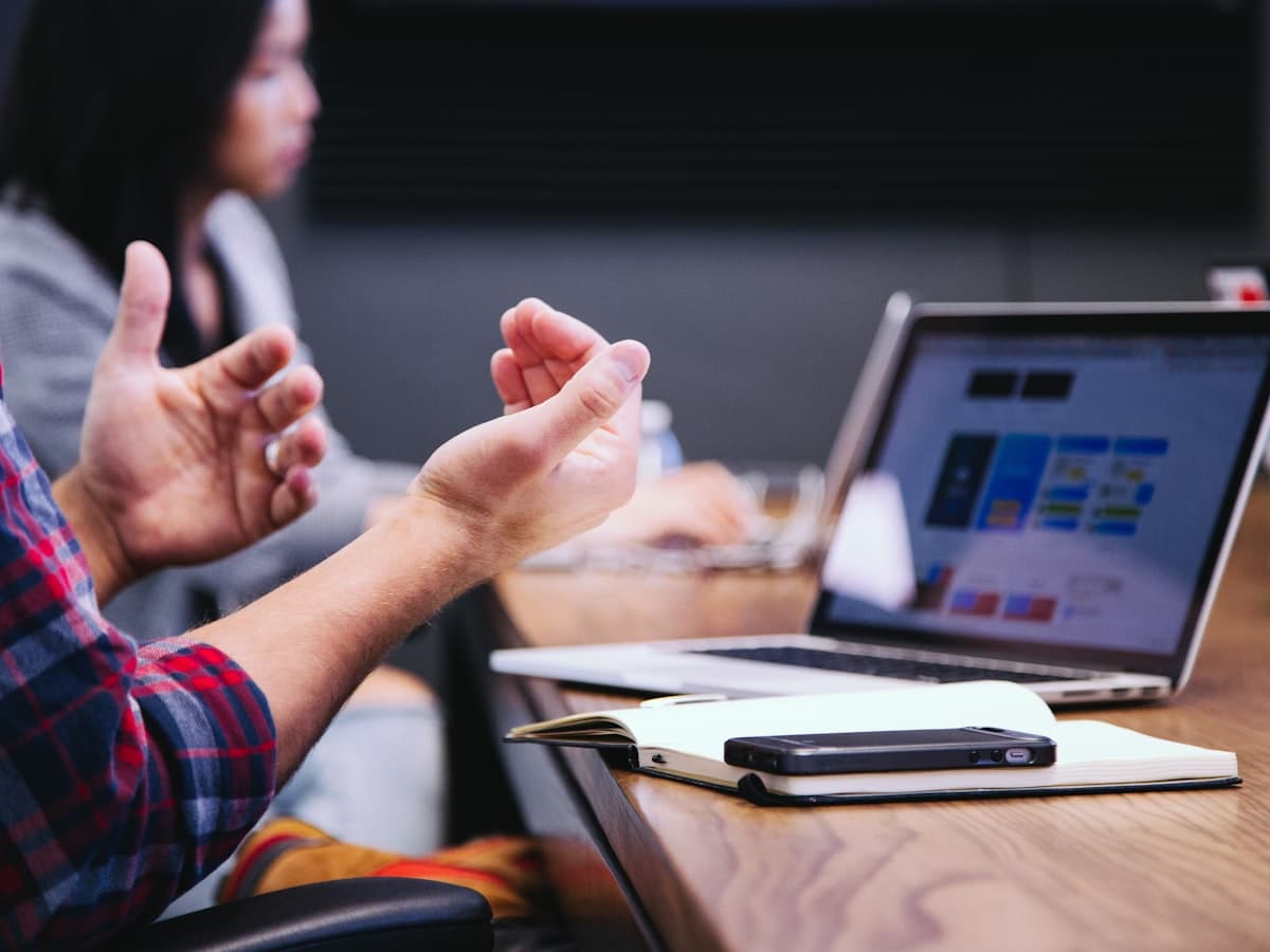 Professionals gesturing and discussing during a meeting, laptop open on the table